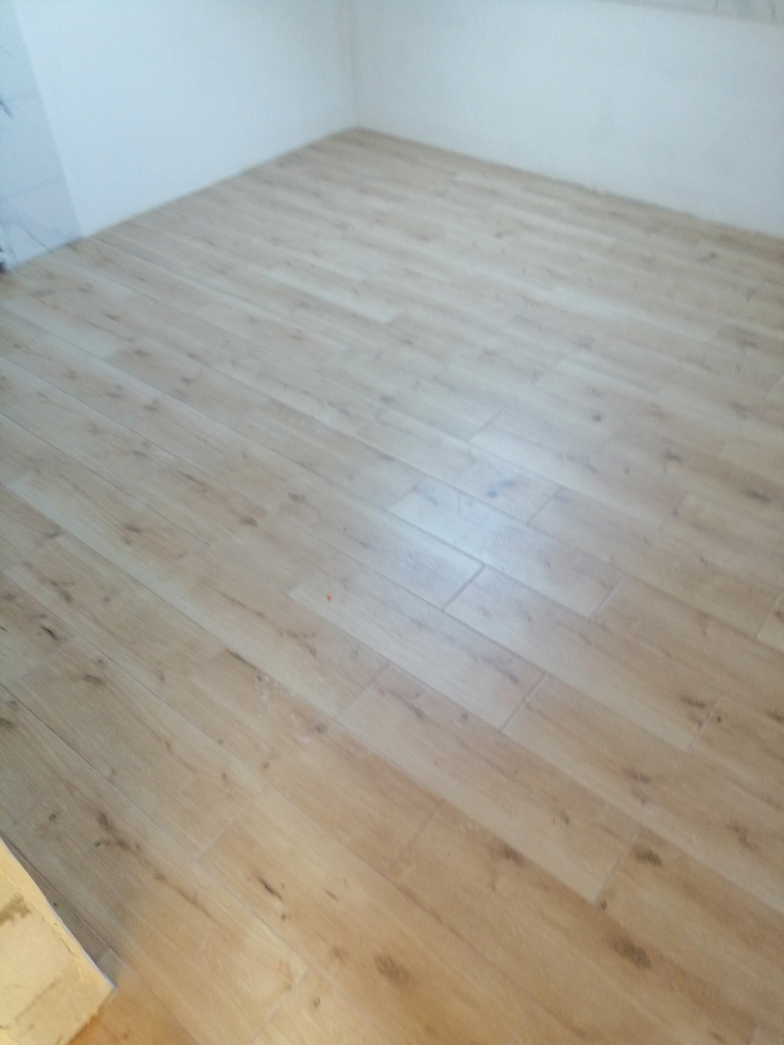 Ukończona podłoga z płytek imitujących drewno ułożonych w prostym wzorze, jasne ściany w tle.