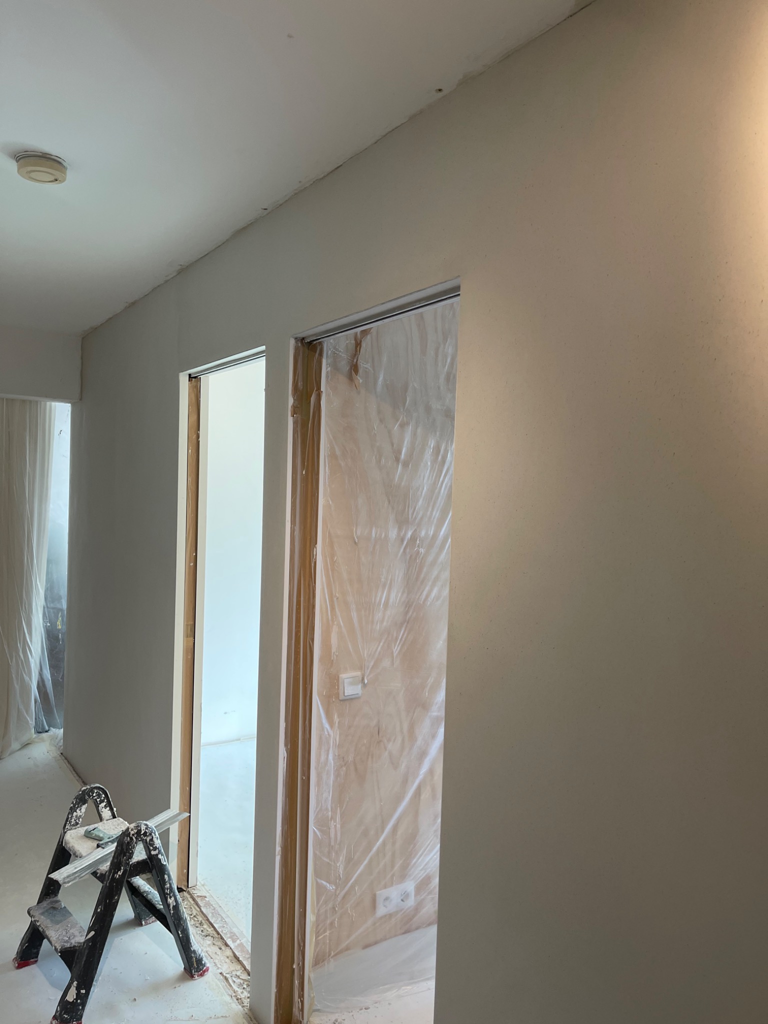 Pokój w trakcie remontu, ściany przygotowane do malowania, widoczna drabina malarska i zabezpieczone folią drzwi.