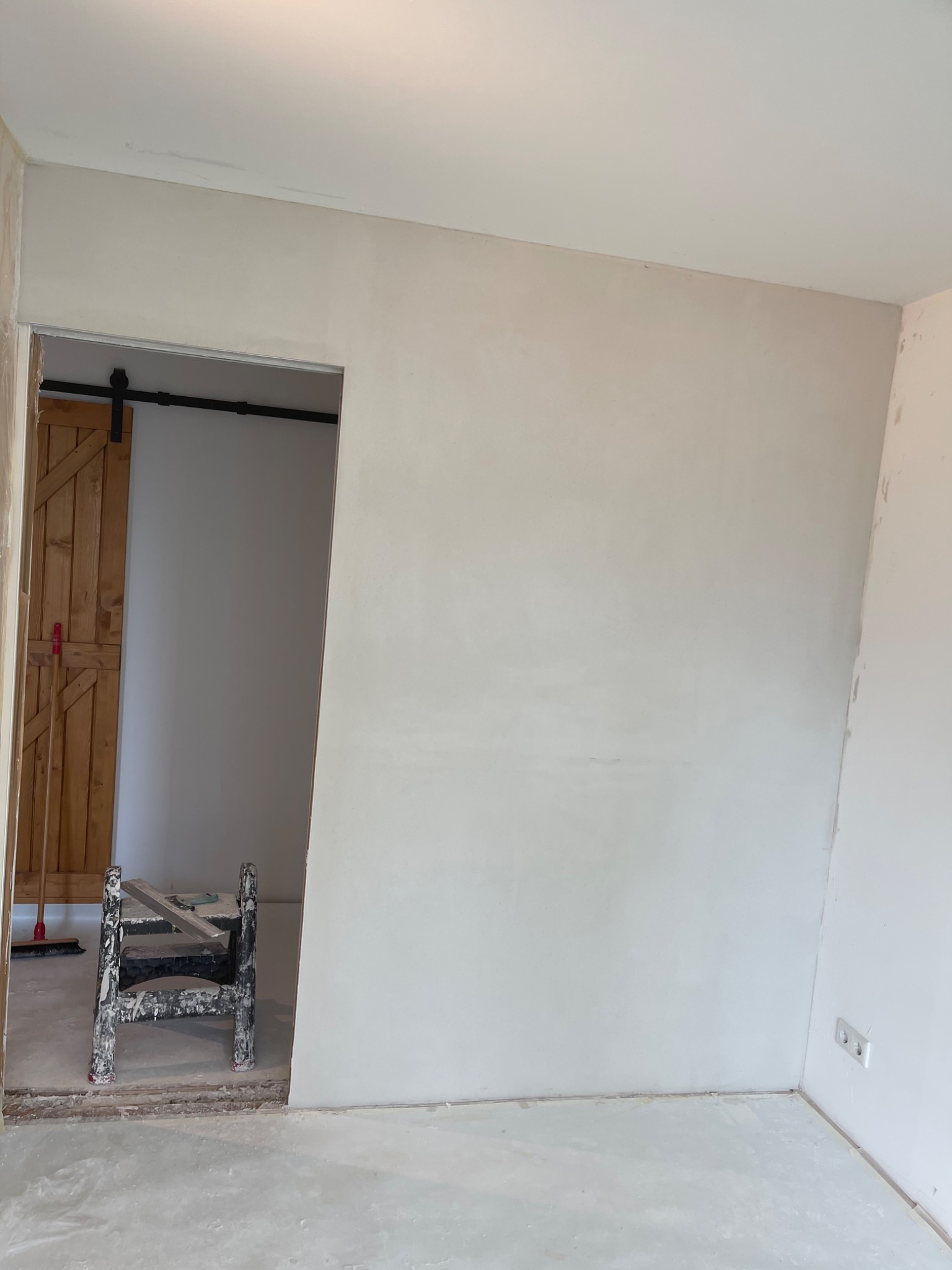 Wnętrze pokoju po szpachlowaniu ścian, widoczna drabinka malarska i drewniane drzwi przesuwne w tle.