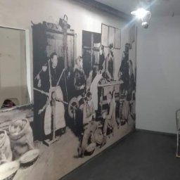 Arteria Studio Wnętrz- usługi remontowe - Korytarz biurowy z fototapetą przedstawiającą scenę z życia wiejskiego, oświetlony lampą sufitową i wyposażony w system przeciwpożarowy.