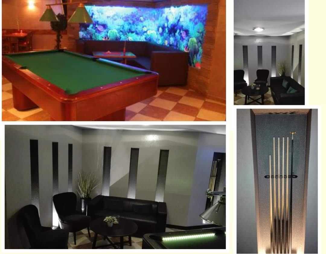 Eleganckie wnętrze pokoju bilardowego w Wejherowie z akcentem w postaci podświetlanego akwarium w ścianie, widoczny stół bilardowy z zielonym suknem oraz zestaw kijów w specjalnym uchwycie.