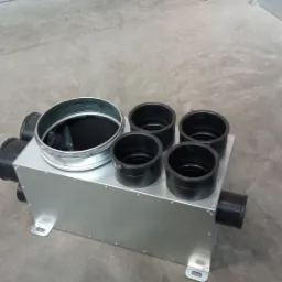 Szara skrzynka rozdzielcza z metalowymi i plastikowymi króćcami na szarym, betonowym tle.