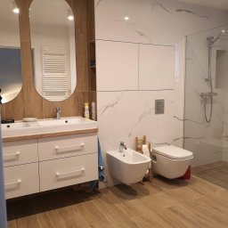 Zizi studio Magdalena Latos - Nowoczesna łazienka z drewnopodobną podłogą, marmurowymi płytkami ściennymi, umywalką z szafką, bidetem, toaletą i kabiną prysznicową ze szklanymi drzwiami.