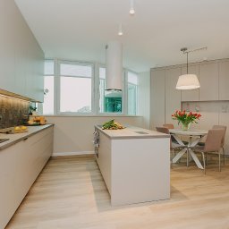 Zizi studio Magdalena Latos - Jasna, nowoczesna kuchnia z wyspą, drewnianą podłogą i stołem z bukietem tulipanów na blacie.