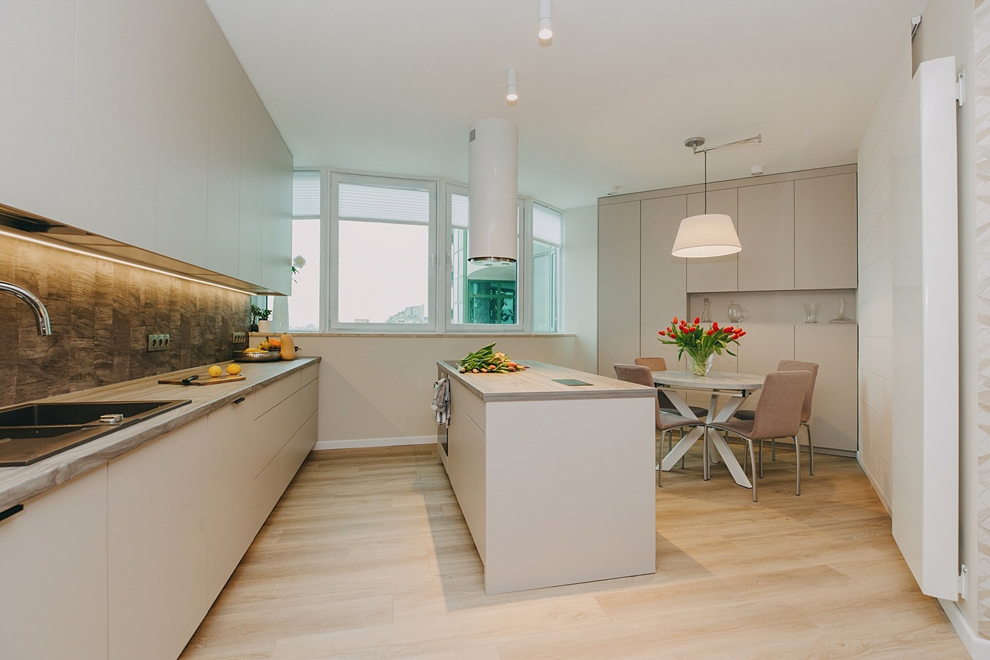 Jasna, nowoczesna kuchnia z wyspą, drewnianą podłogą i stołem z bukietem tulipanów na blacie.