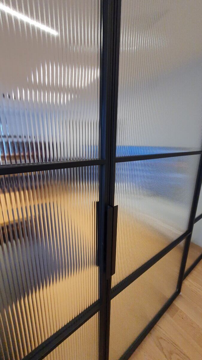 Nowoczesne, dwuskrzydłowe przeszklenie z ryflowanego szkła w czarnej ramie, widok z bliska na klamkę i strukturę szkła.