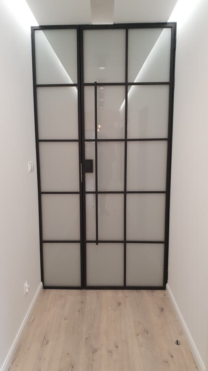 Nowoczesne dwuskrzydłowe przesuwne drzwi w stylu loft z czarną ramą i mlecznym szkłem, widoczne w korytarzu z panelami podłogowymi i oświetleniem LED na suficie.