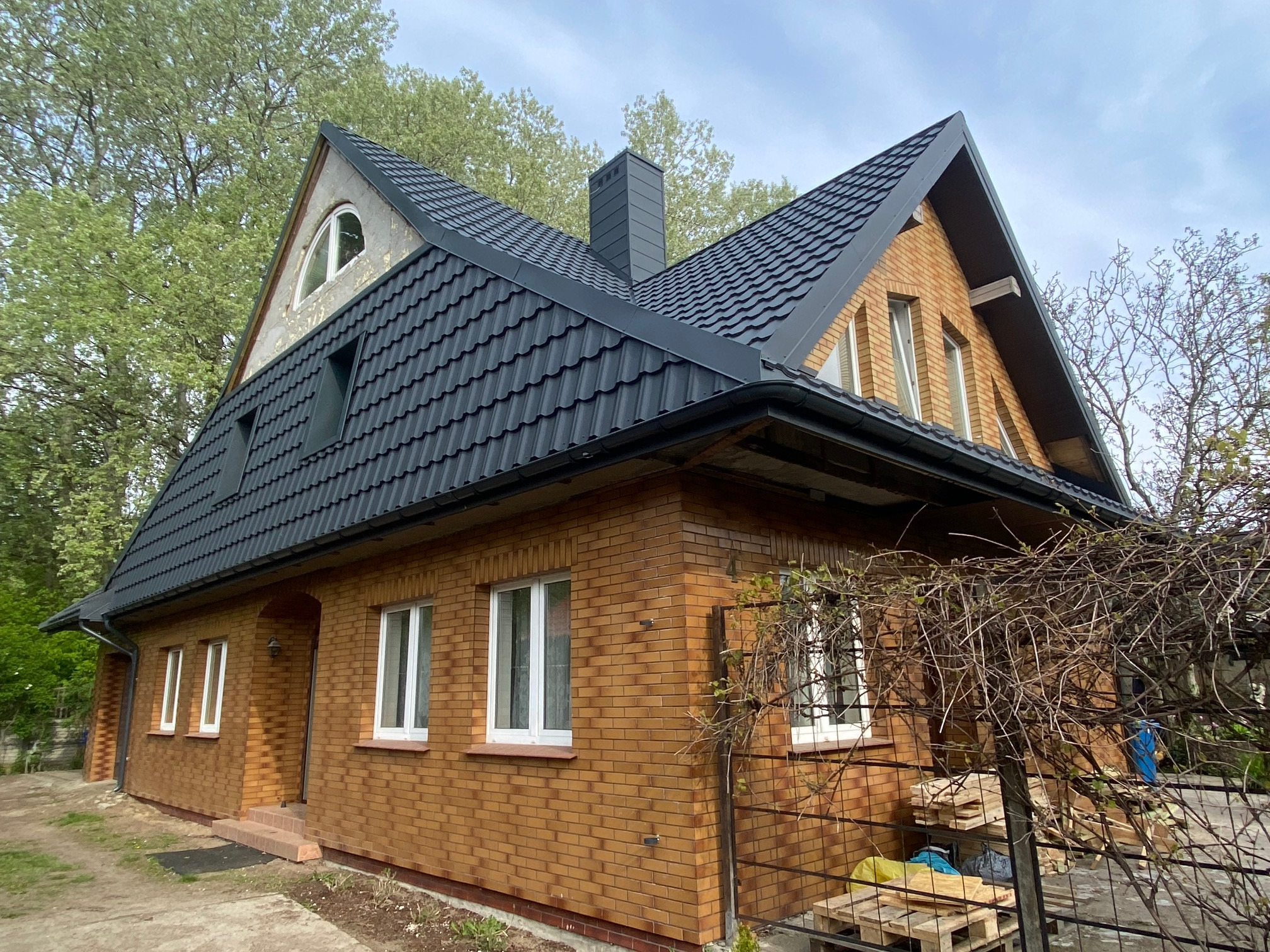 Dom jednorodzinny z ciemną dachówką ceramiczną, ceglaną elewacją i kominem w kolorze dachu, widok z zewnątrz w słoneczny dzień.