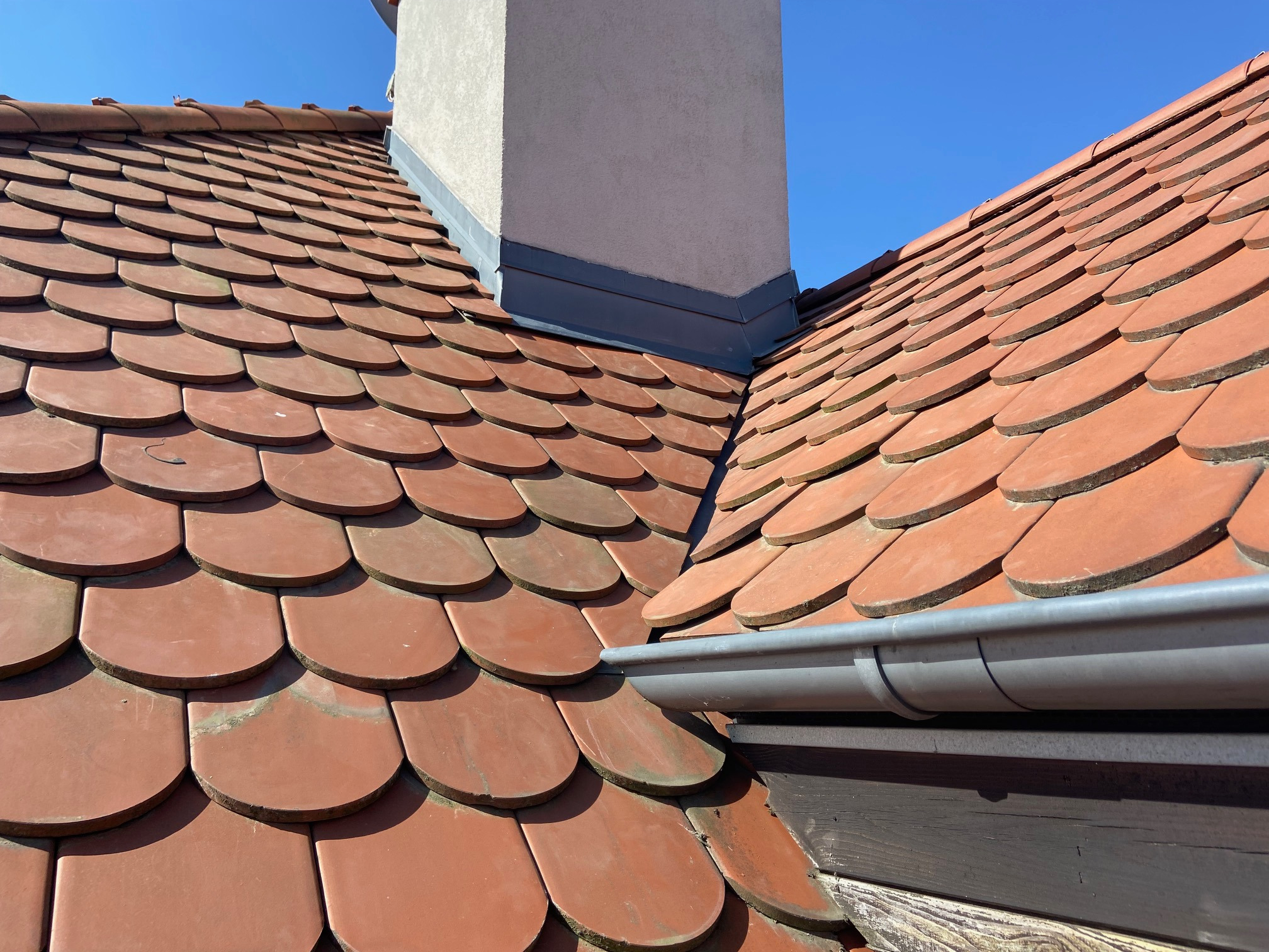 Dachówka karpiówka w odcieniach czerwieni, z widocznym kominem i szarą rynną, na tle błękitnego nieba.