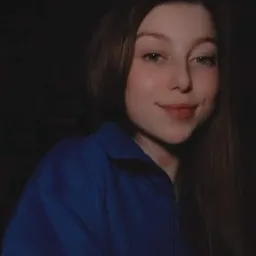 Portret uśmiechniętej dziewczyny w niebieskiej bluzie na ciemnym tle, z widocznym dołeczkiem w policzku.