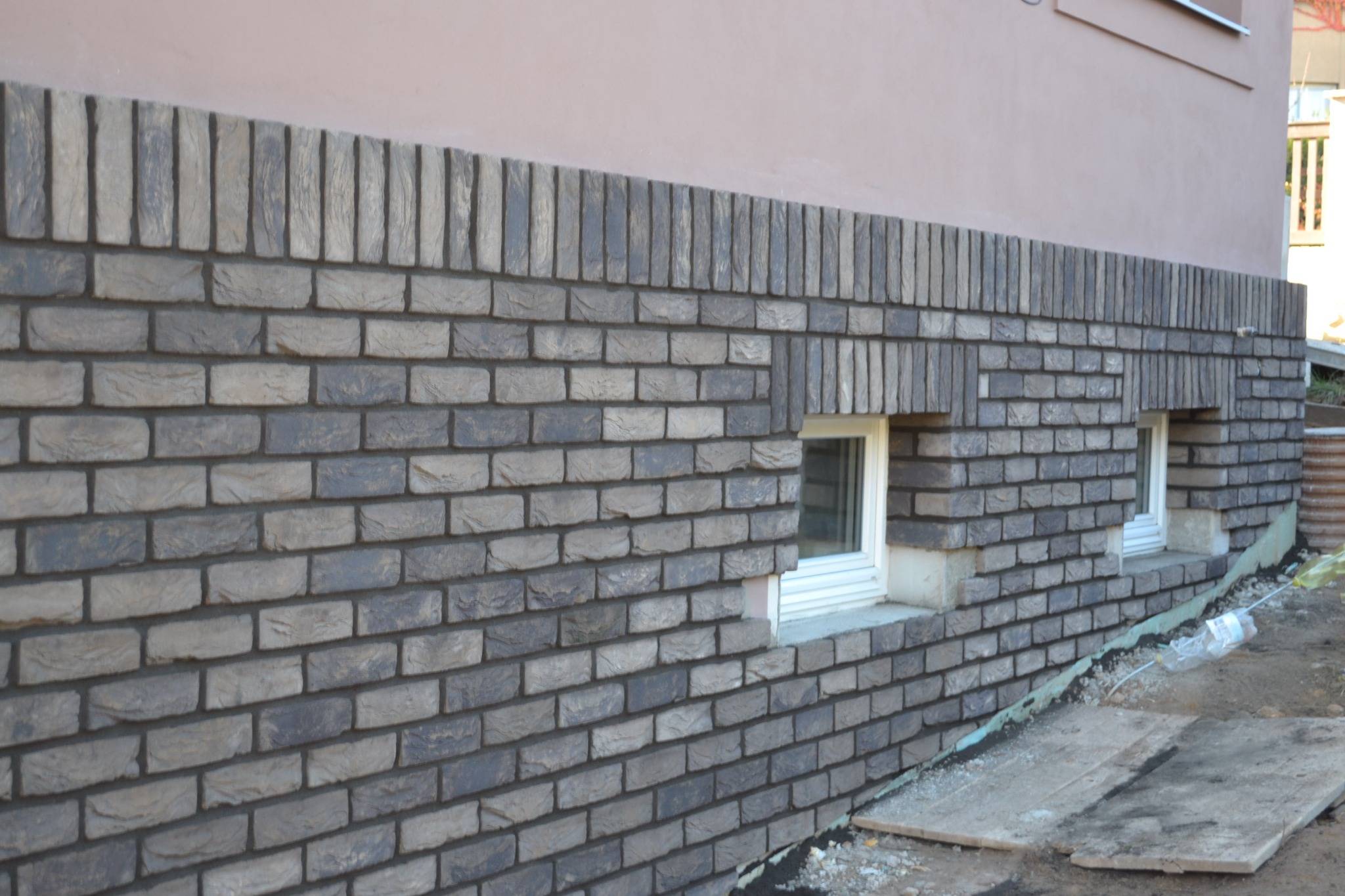 Nowa elewacja z szarej cegły klinkierowej wokół okien piwnicznych, widoczne detale wykończenia i izolacja przy gruncie.