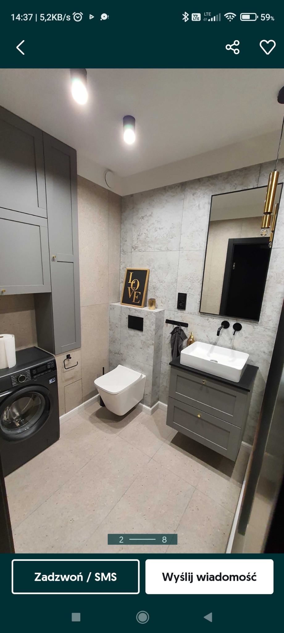 Nowoczesna łazienka w szarościach z wiszącą toaletą, umywalką nablatową na szafce z szufladami i pralką automatyczną, wykończona płytkami imitującymi kamień, z dodatkami w kolorze złota.