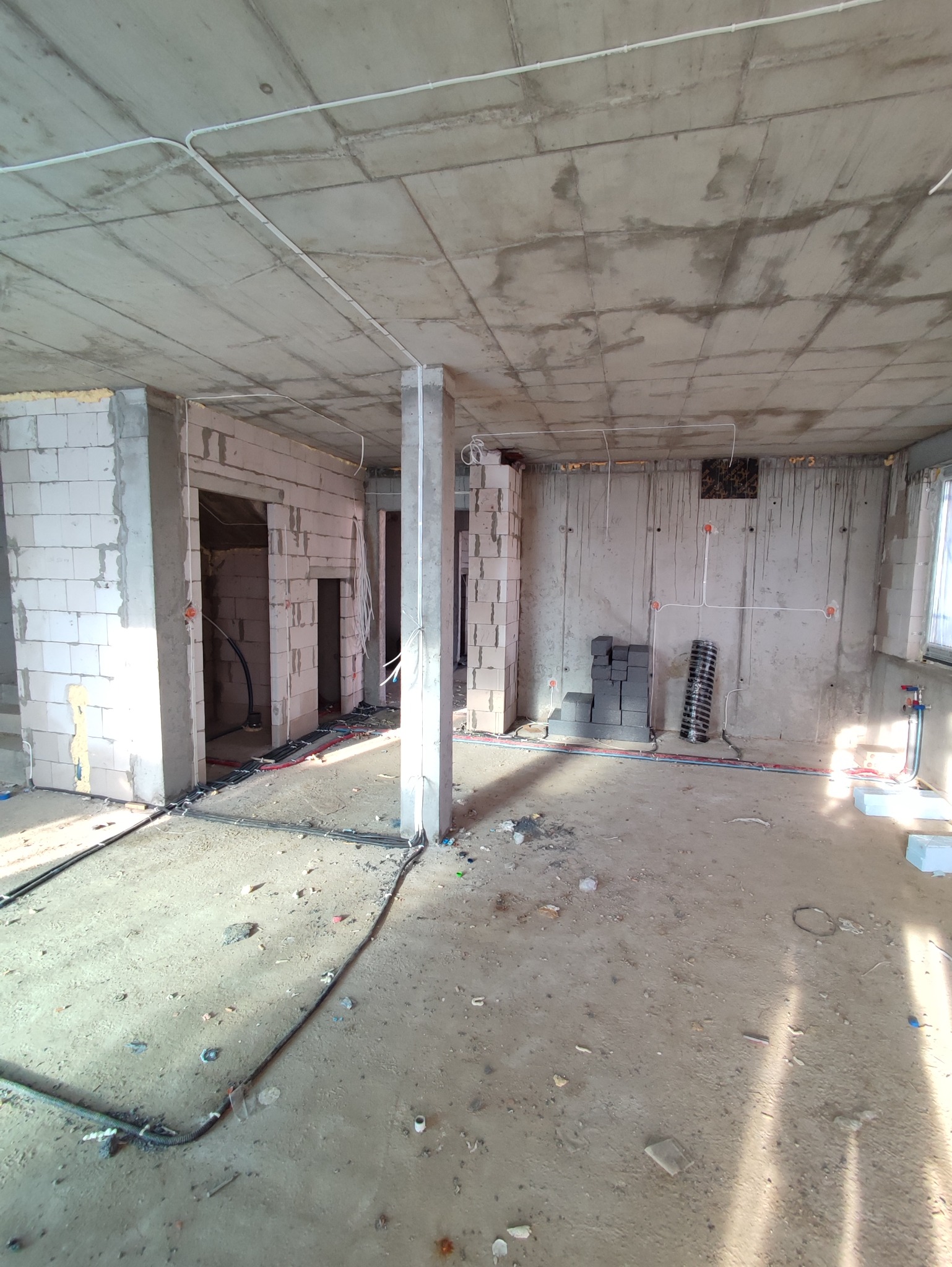 Surowy stan wnętrza w trakcie budowy, widoczne instalacje elektryczne w peszlach na podłodze i pod sufitem, ściany z betonu komórkowego i surowego betonu, przygotowane punkty elektryczne