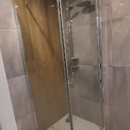 Nowoczesna kabina prysznicowa z deszczownicą i szklaną ścianką na tle szarych płytek w wyremontowanej łazience.