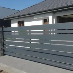 Szara, przesuwna brama wjazdowa z poziomych profili na tle nowoczesnego domu z szarą dachówką i kostką brukową.