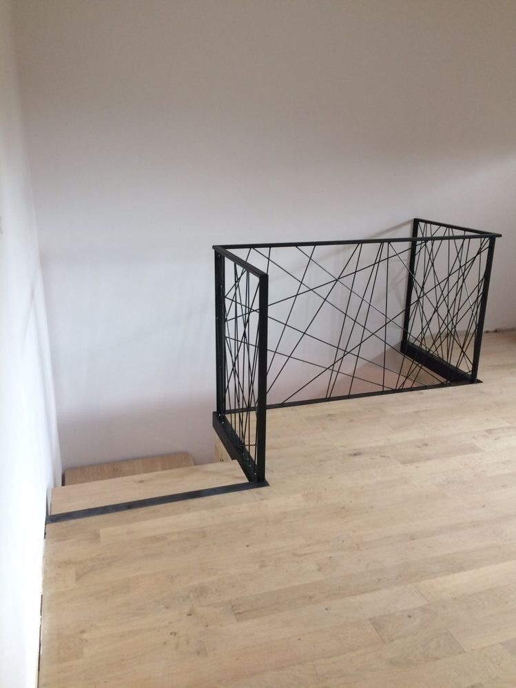 Czarna, metalowa balustrada schodowa z geometrycznym wzorem z cienkich prętów w Imielinie, zamontowana na jasnej drewnianej podłodze przy schodach.