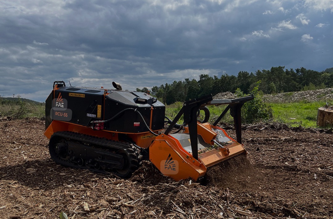 Automatyczna frezarka do pni FAE RCU-55 na gąsienicach, rozdrabniająca ścięte drewno na mulcz na terenie po wycince, z widocznym pniem w tle i zachmurzonym niebem.