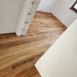 Ukończona podłoga z paneli drewnianych w skosie, z widocznym fragmentem ściany z betonu komórkowego i listwami przypodłogowymi, w jasnym pomieszczeniu.