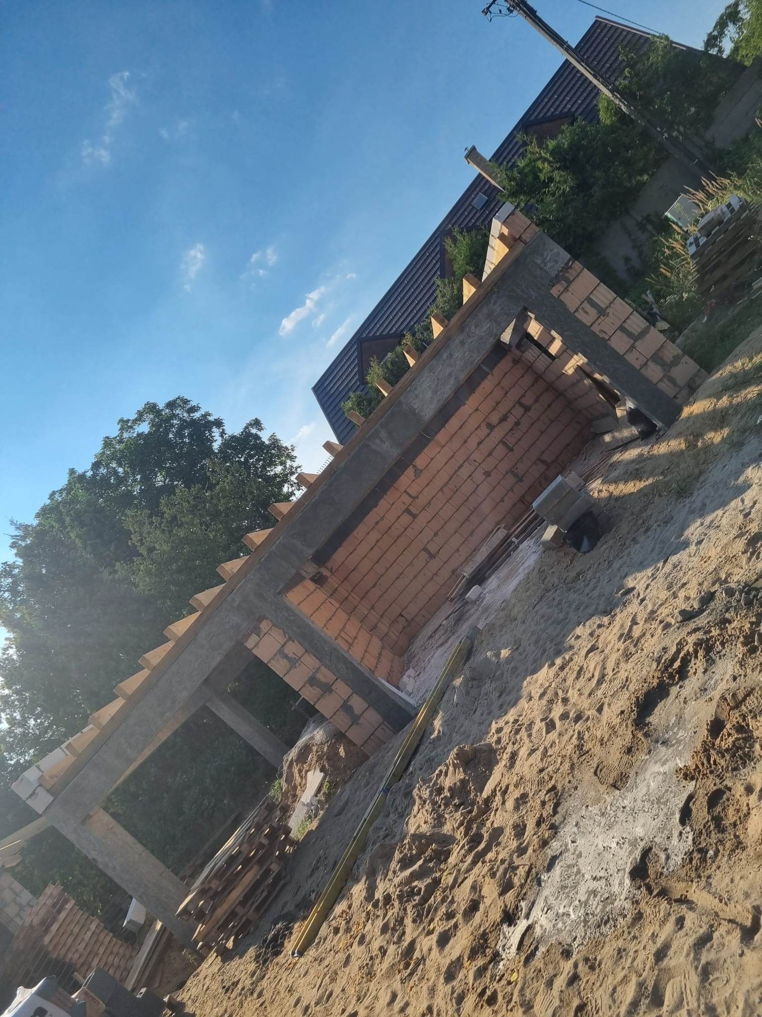 Murowana konstrukcja poddasza z betonu i cegieł, widok z dołu na tle błękitnego nieba i drzew, w otoczeniu piasku.