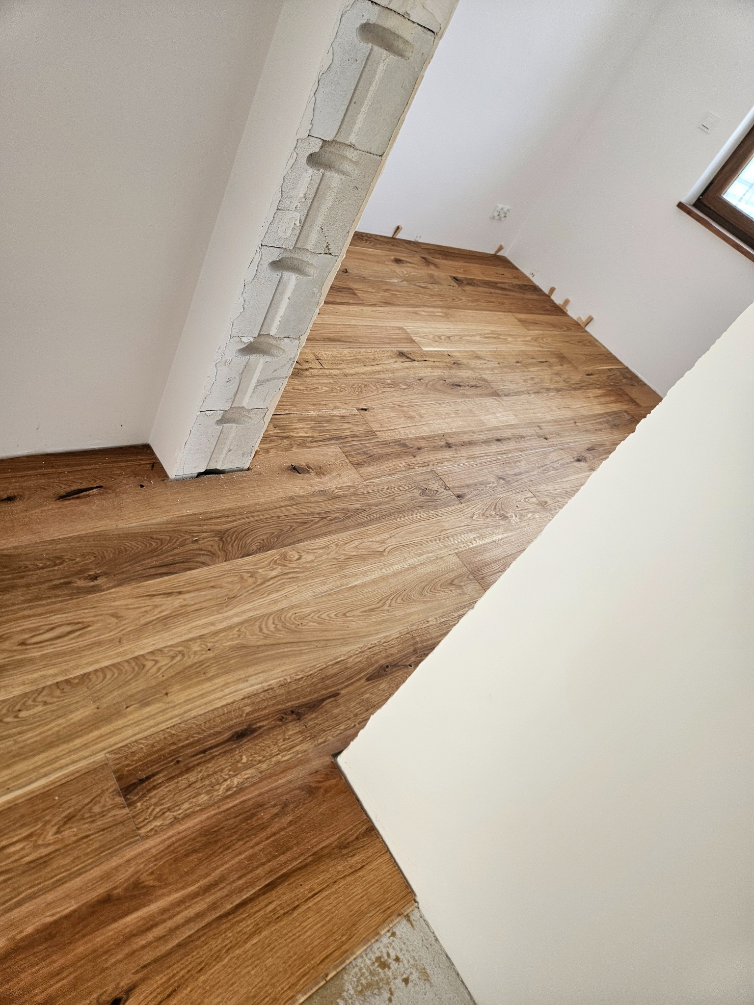 Ukończona podłoga z paneli drewnianych w skosie, z widocznym fragmentem ściany z betonu komórkowego i listwami przypodłogowymi, w jasnym pomieszczeniu.