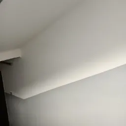 Świeżo pomalowana klatka schodowa, widok z góry na szare ściany i biały sufit, schody z ciemnym wykończeniem u dołu kadru.