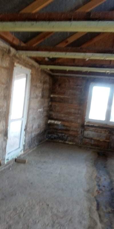 Poddasze w trakcie prac remontowych, widoczne drewniane belki stropowe, ściany przygotowane do dalszych prac wykończeniowych, z oknem i drzwiami.