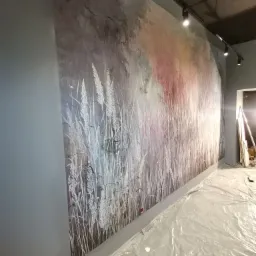 Ściana z szarą tapetą w motywie łąki z białymi źdźbłami, podłoga zabezpieczona folią malarską, oświetlenie punktowe sufitowe.