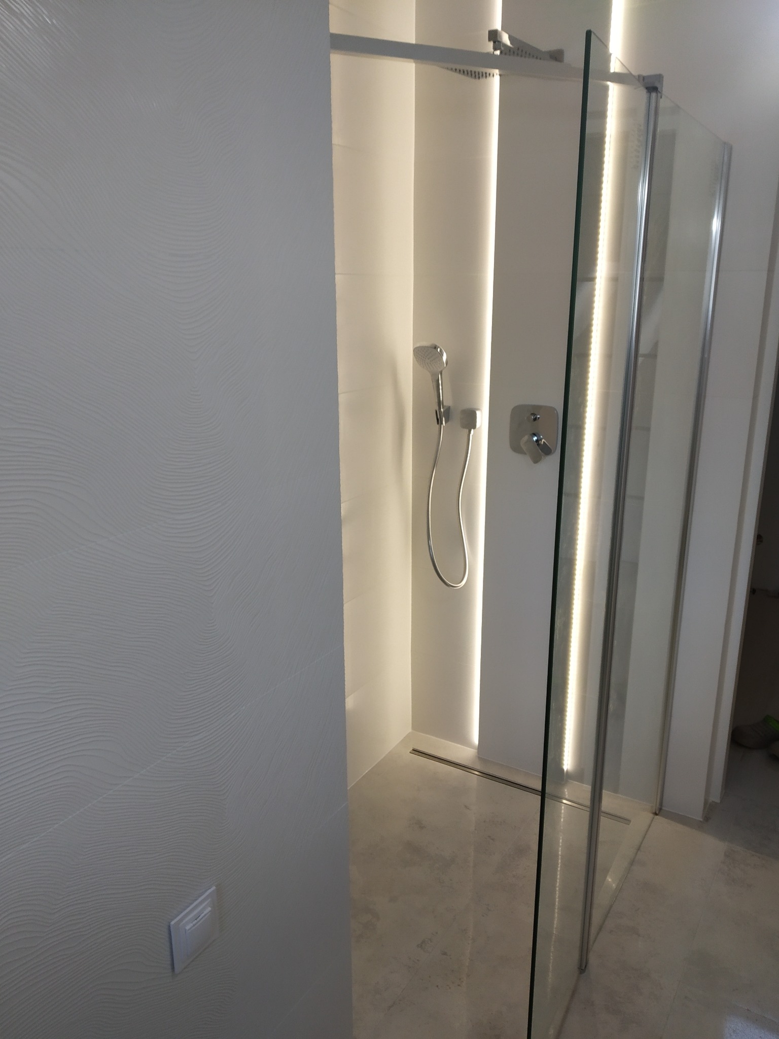 Nowoczesna kabina prysznicowa z deszczownicą i oświetleniem LED, wykończona płytkami z subtelnym wzorem fal. Minimalistyczny design, chromowane elementy.