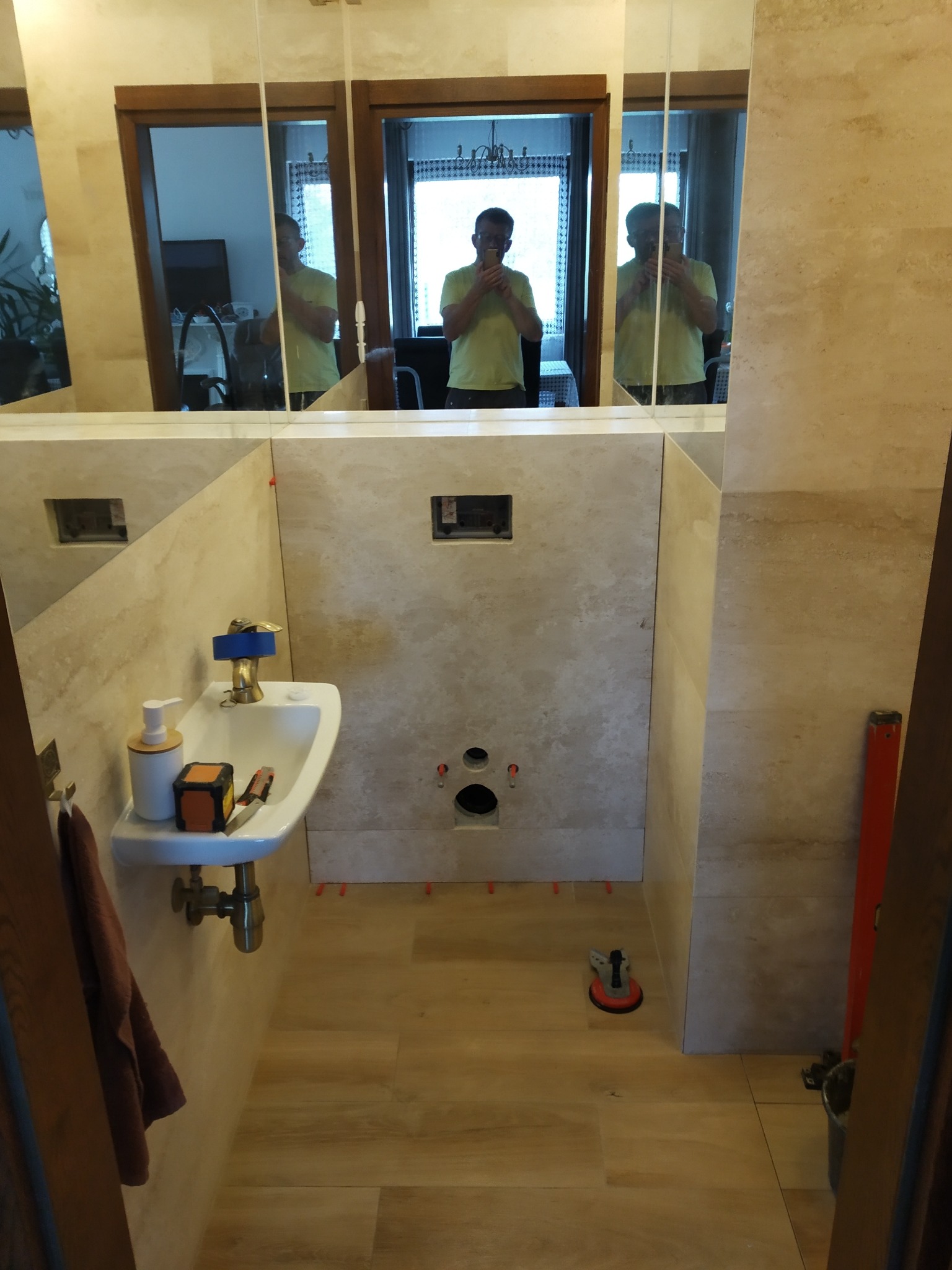 Wnętrze łazienki w trakcie remontu: ułożone płytki na ścianach i podłodze, widoczne narzędzia glazurnicze, odbicie osoby robiącej zdjęcie w lustrze.