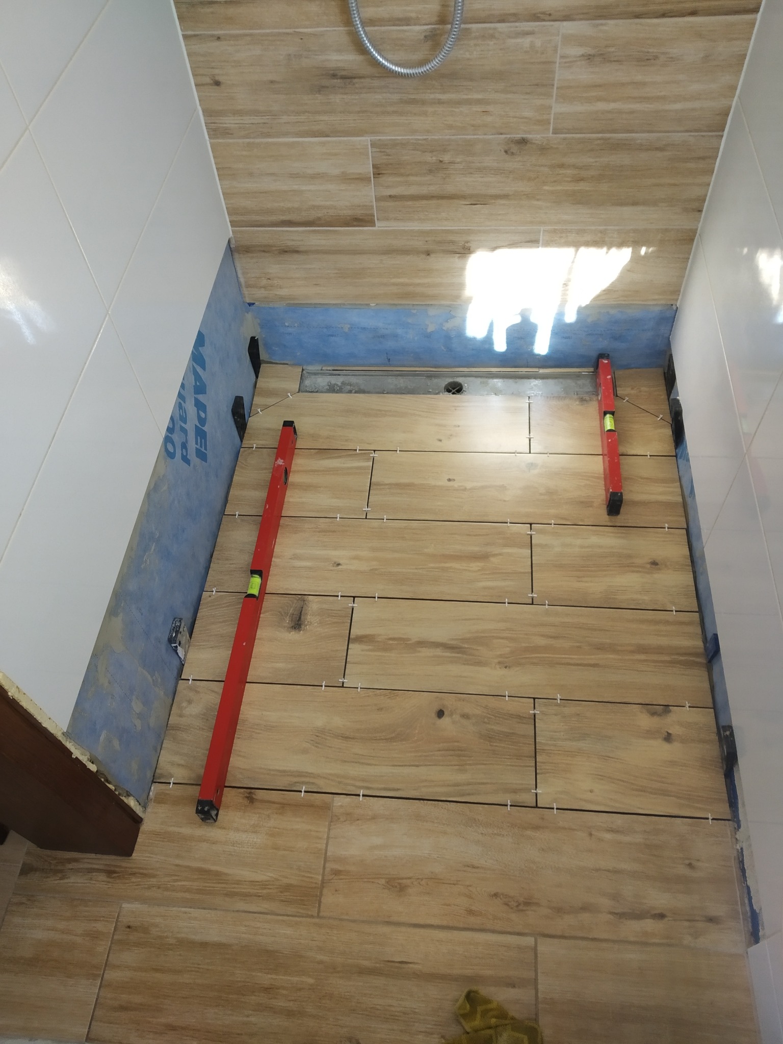 Układanie płytek imitujących drewno w kabinie prysznicowej. Widoczne poziomice, krzyżyki dystansowe i hydroizolacja na ścianach. Etap prac przed fugowaniem.