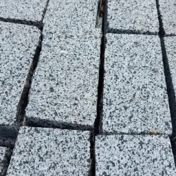 Szare, prostokątne elementy nawierzchni ułożone blisko siebie, z widocznymi drobnymi nierównościami i szorstką fakturą.