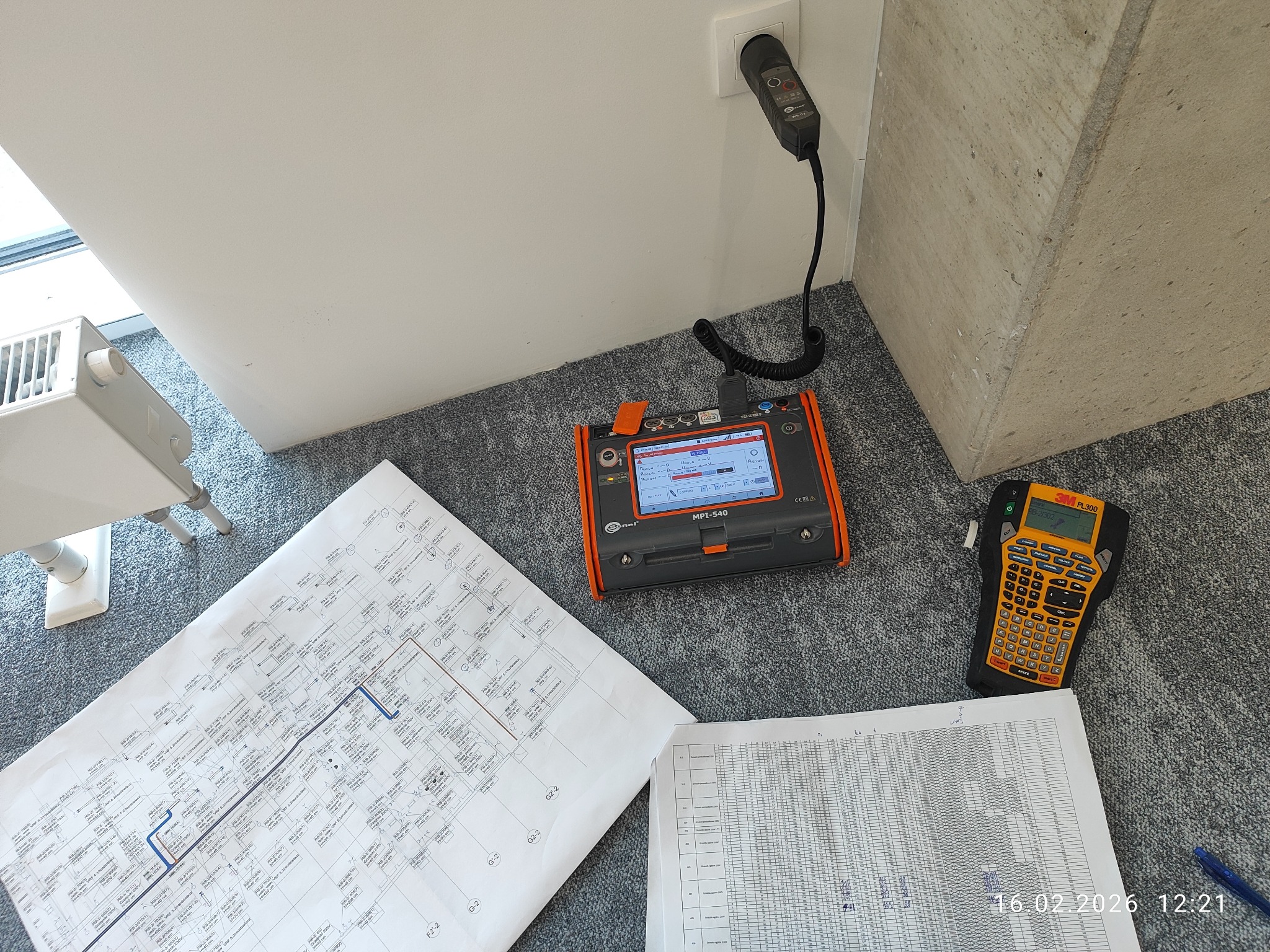 Miernik MPI-540 Sonel podłączony do gniazdka, obok schemat instalacji, etykietownica 3M PL300 i arkusz z danymi pomiarowymi na szarym dywanie.
