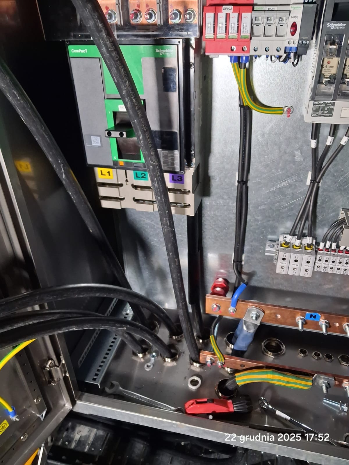 Rozdzielnica elektryczna w trakcie montażu: widoczne kable, zabezpieczenia, listwy zaciskowe i narzędzia. Elementy oznaczone L1, L2, L3 i N.