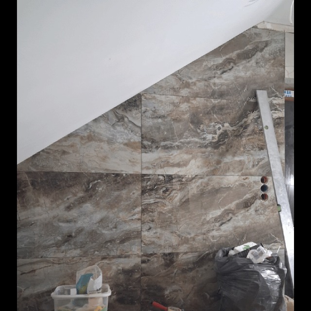 Ukończona ściana z płytek imitujących marmur, ułożonych pod skosem, z widocznymi otworami na gniazdka i narzędziami w tle. Wykończenie wnętrza.