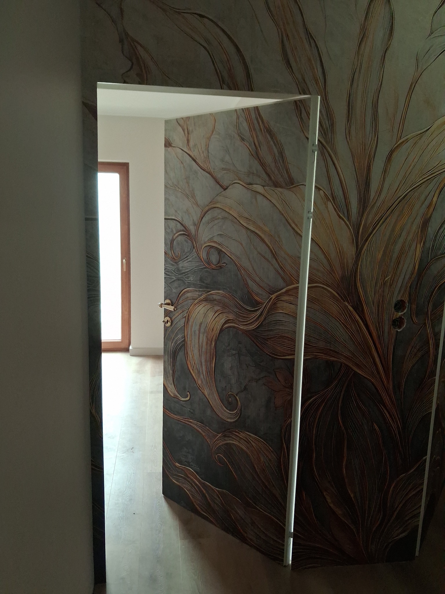 Otwarta, dekoracyjna, wewnętrzna stolarka drzwiowa z motywem roślinnym na tle ściany z identycznym wzorem, tworząca spójną aranżację wnętrza.