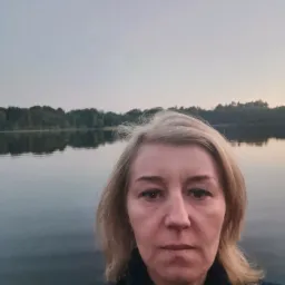 Portret kobiety z blond włosami na tle jeziora i lasu o zmierzchu.
