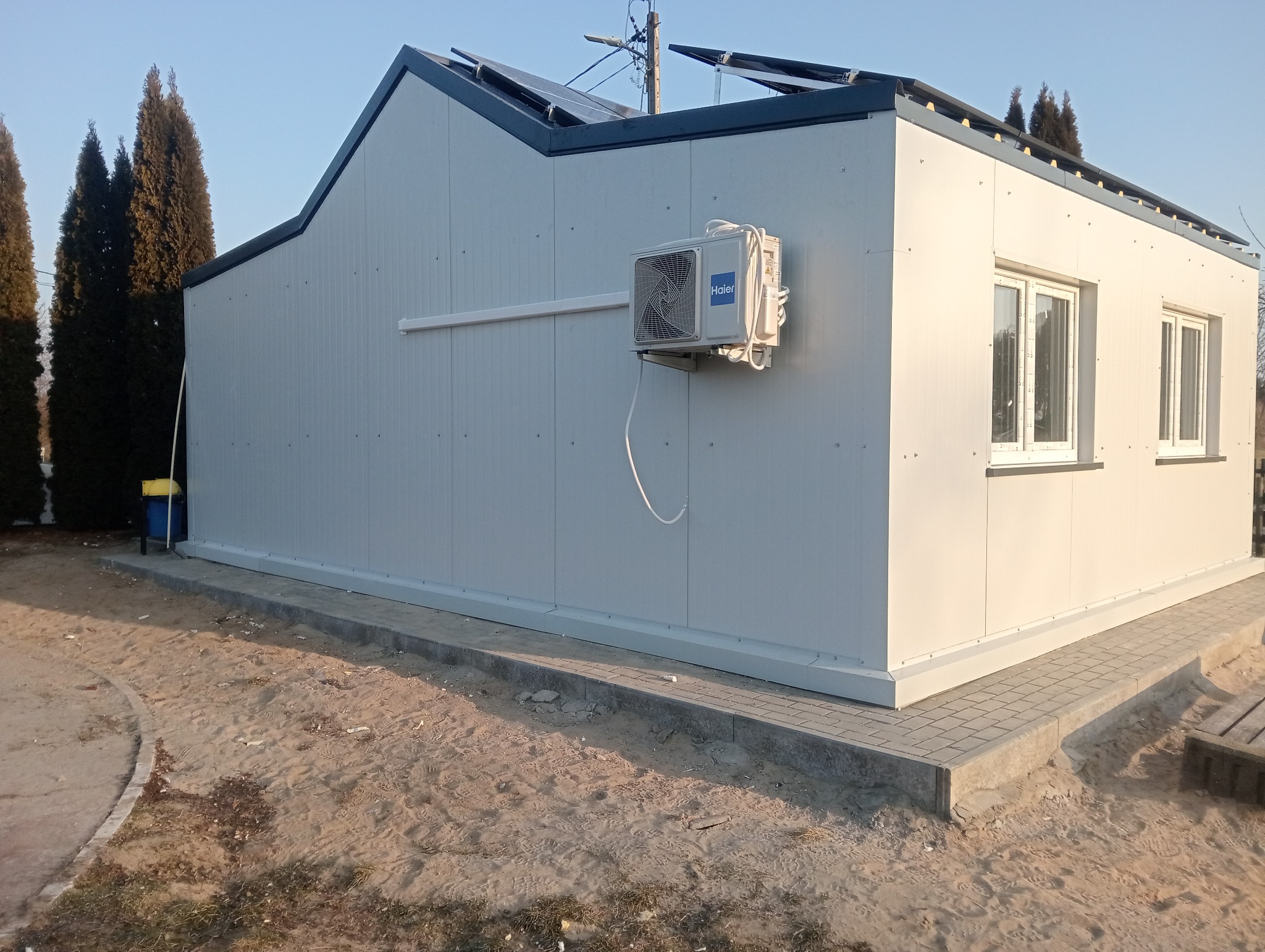 Gotowa hala z płyt warstwowych z klimatyzatorem Haier na zewnątrz, widoczne panele słoneczne na dachu.