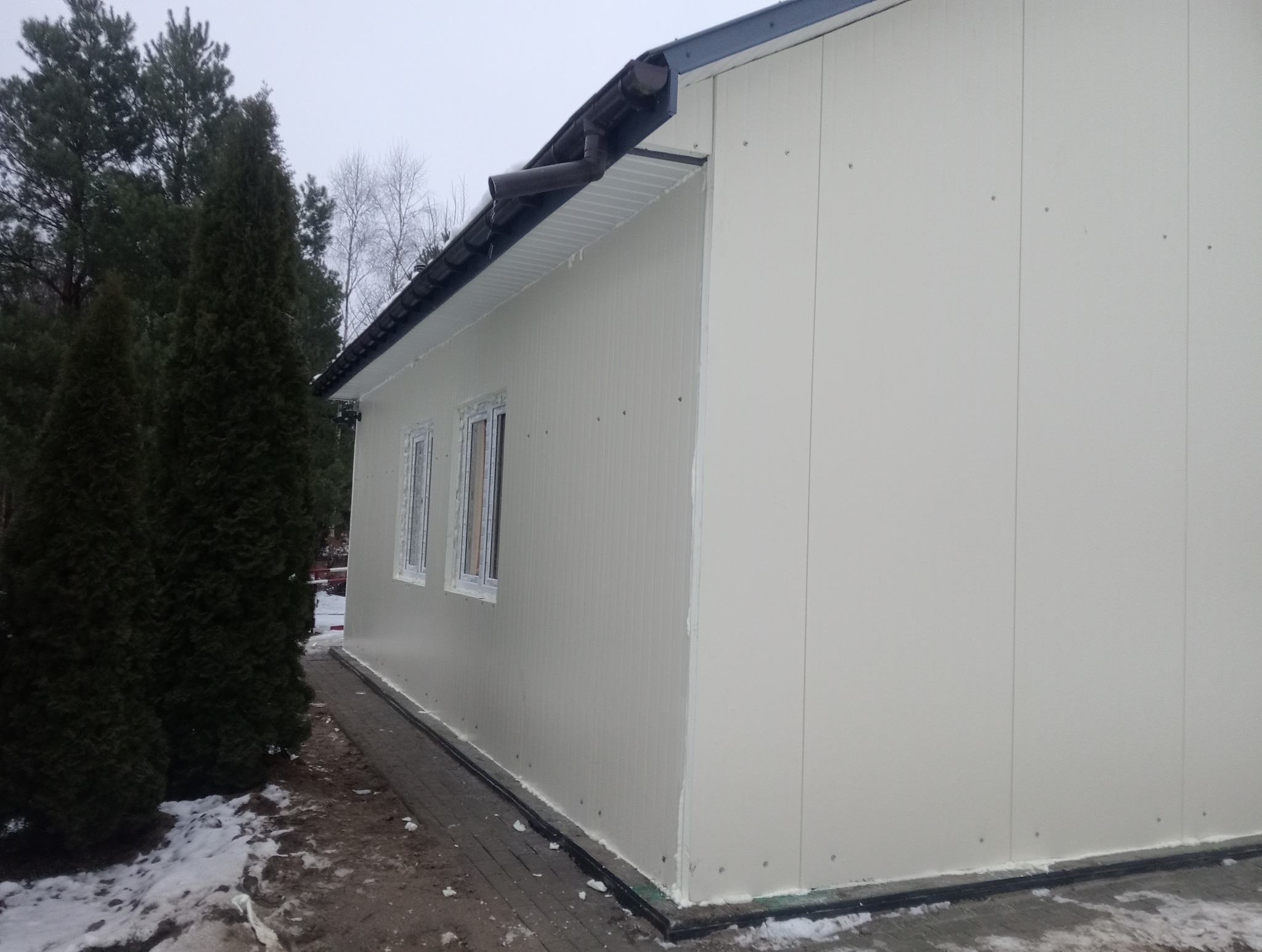 Gotowa hala z płyt warstwowych w zimowej scenerii, widoczne dwa okna i ciemna rynna