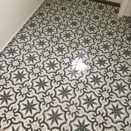 Nowa podłoga z wzorzystych, czarno-białych płytek ceramicznych w małym pomieszczeniu, widok z góry, z delikatnym odbiciem światła na powierzchni.