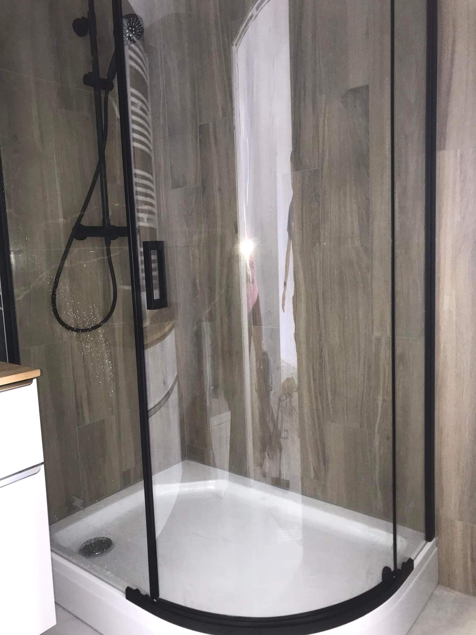 Nowoczesna kabina prysznicowa z czarnymi profilami, deszczownicą i panelami imitującymi drewno na ścianach.