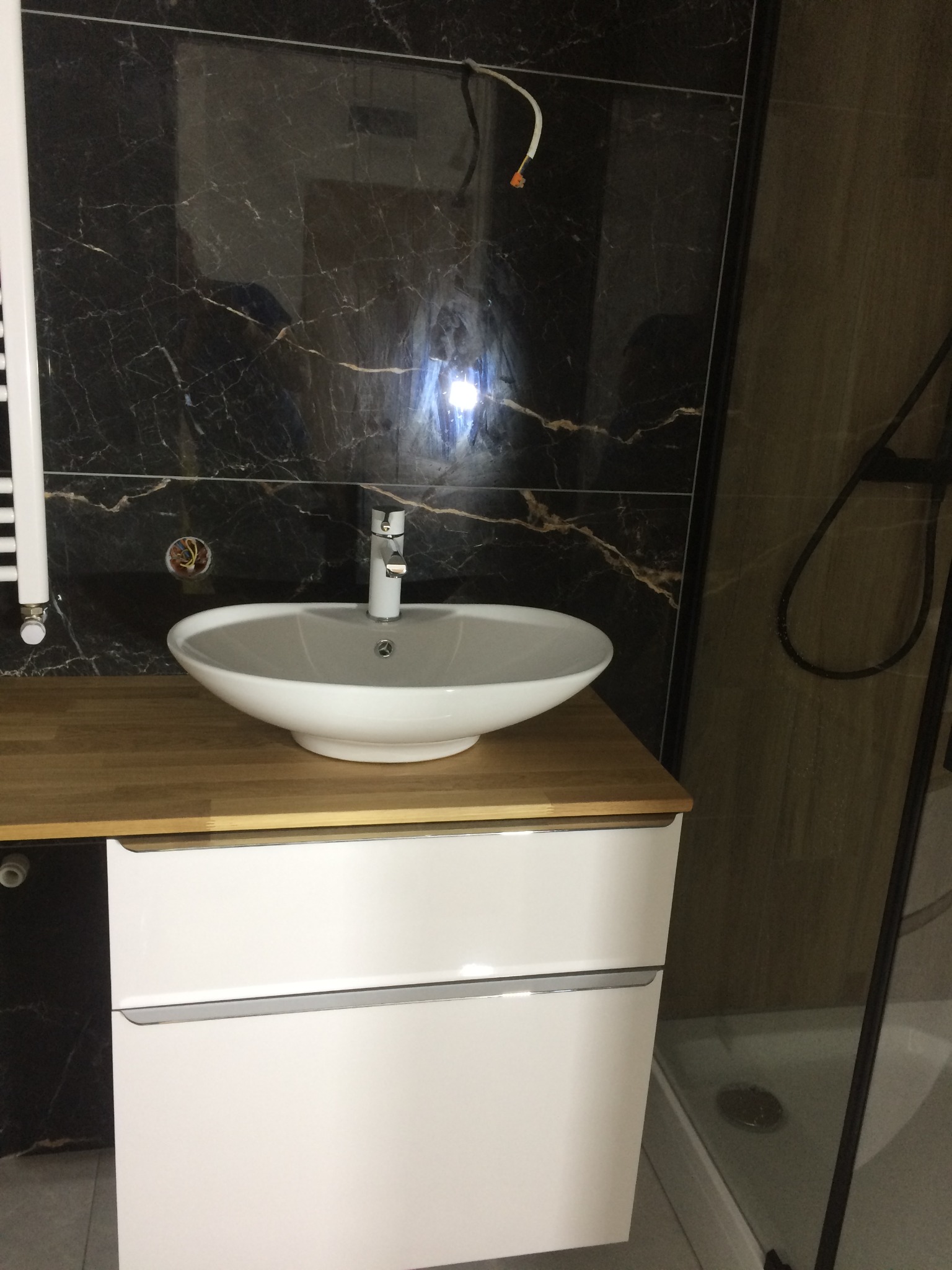 Umywalka nablatowa w łazience po remoncie w Karnicach, z czarnymi płytkami imitującymi marmur i drewnianym blatem. Widoczne niedokończone podłączenie elektryczne.