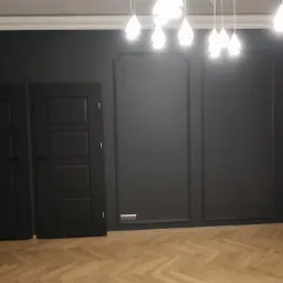 Eleganckie, ciemnoszare wnętrze po remoncie w Warszawie: trzy drzwi wewnętrzne, dekoracyjne listwy ścienne, parkiet w jodełkę i biały grzejnik.