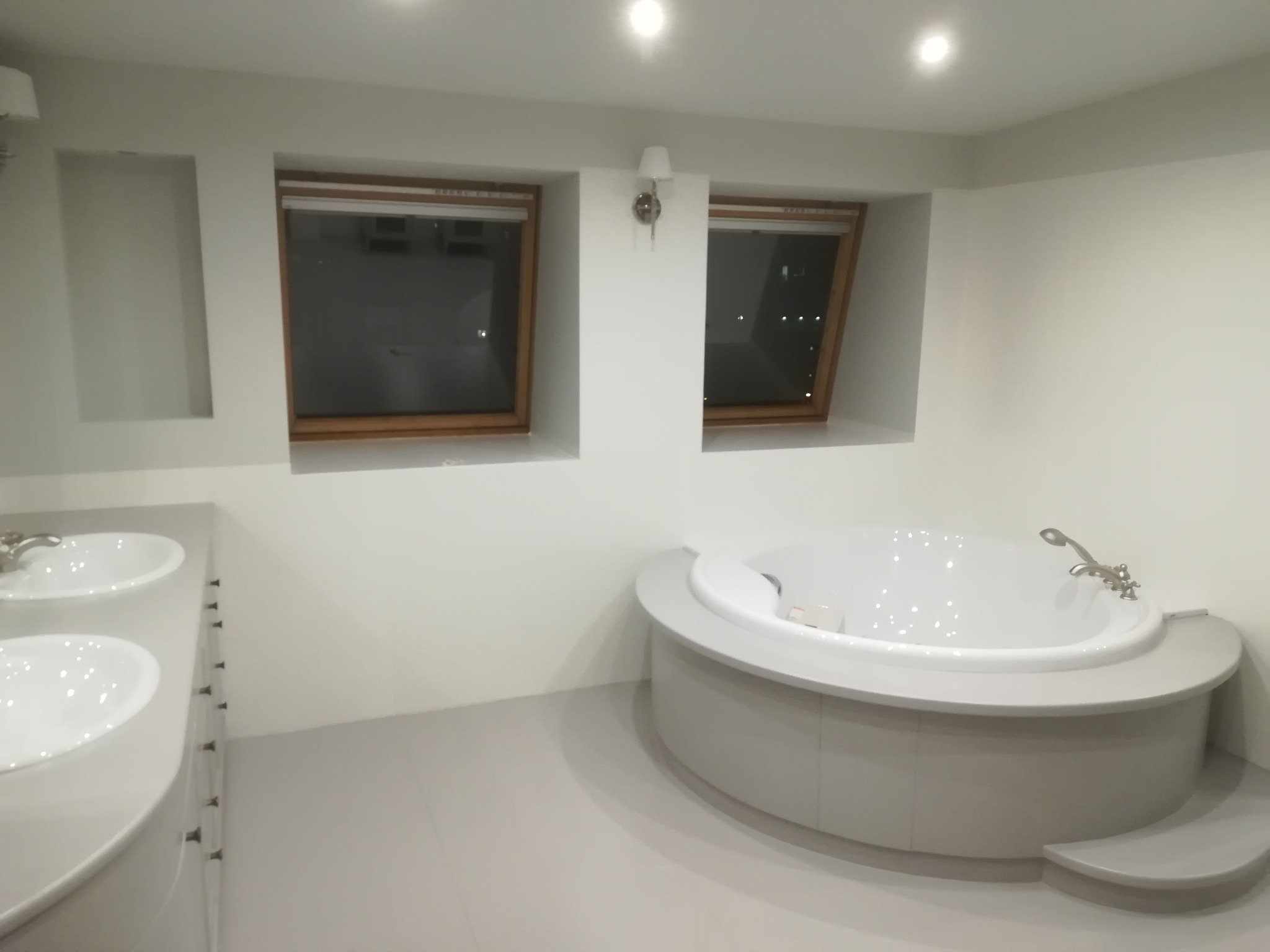 Jasna łazienka z dwoma oknami dachowymi, okrągłą wanną z hydromasażem i podwójną umywalką nablatową na szafce z szufladami.