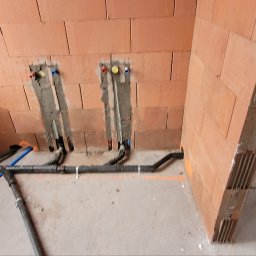 WILK.ins - Surowe ściany z cegły z przygotowanymi otworami na instalację wodno-kanalizacyjną. Widoczne rury w kolorze czarnym i niebieskim, częściowo zamocowane do ściany. Na ścianie widoczne ślady po...