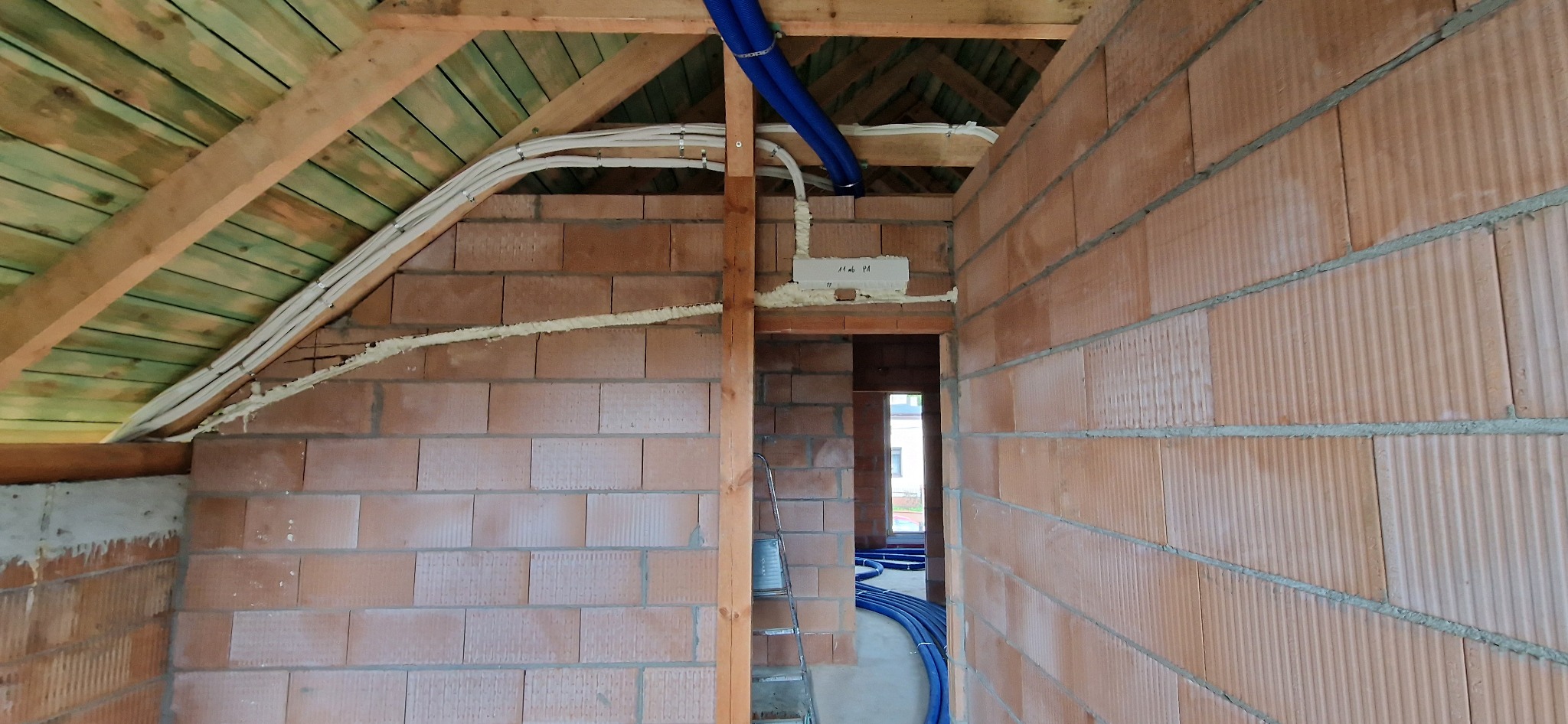 Wnętrze w trakcie budowy z widocznymi instalacjami: rurami wentylacyjnymi i przewodami elektrycznymi, zabezpieczonymi pianką montażową.