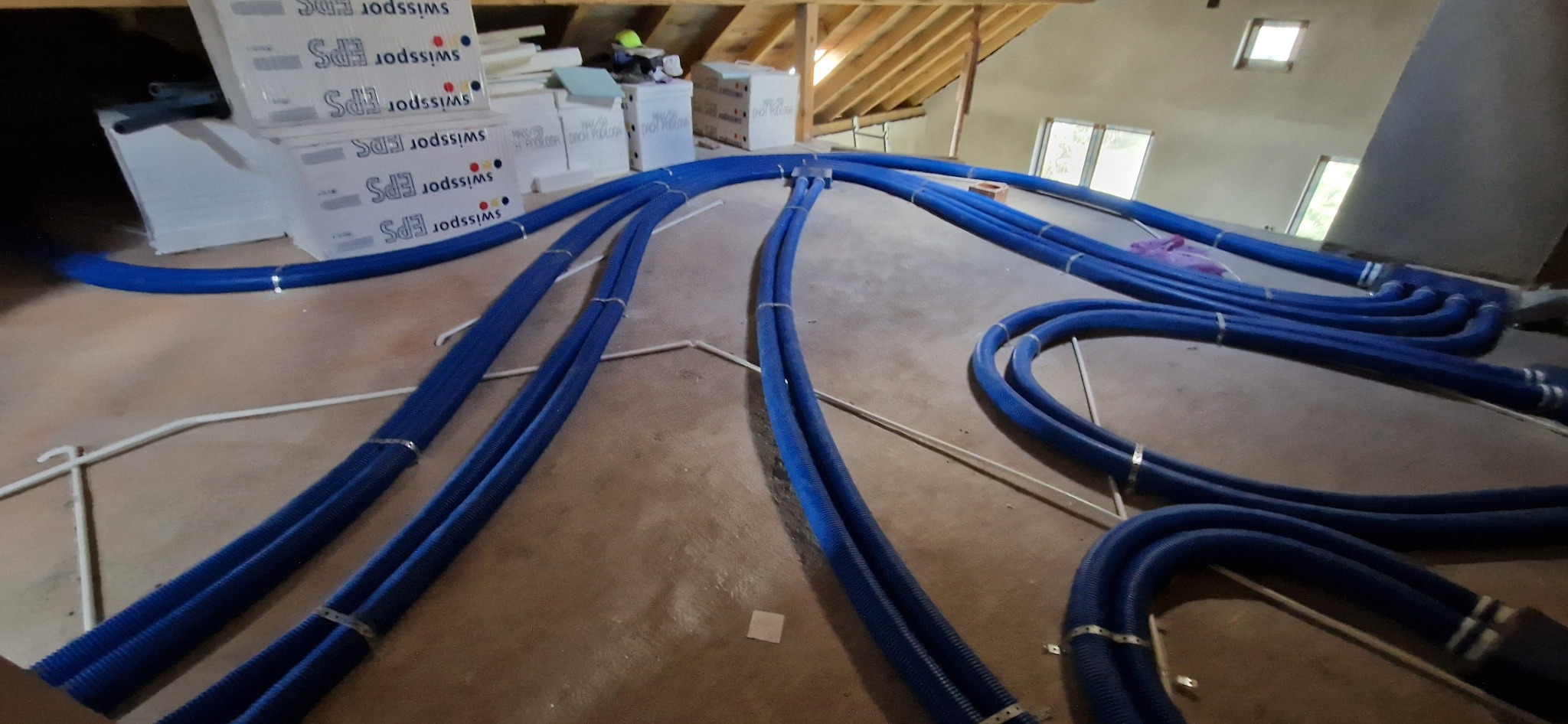 Niebieskie rury wentylacyjne na poddaszu w trakcie montażu, widoczne materiały izolacyjne EPS i drewniana konstrukcja dachu.