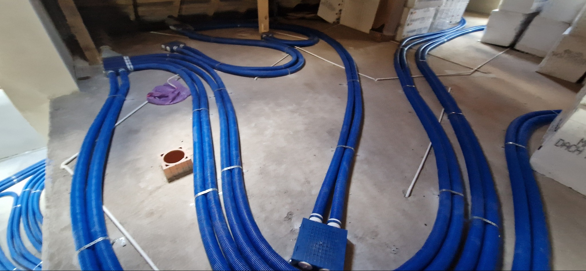 Niebieskie, karbowane rury wentylacyjne ułożone na podłodze w surowym wnętrzu, przed zakryciem instalacji. Widoczne złącza i mocowania.