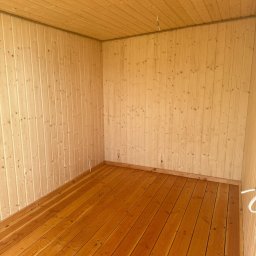 Stolkra - Wnętrze drewnianej konstrukcji z boazerią i podłogą z desek, świeżo po montażu, widok z narożnika, jasne oświetlenie, surowy stan wykończenia.