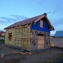 Stolkra - Budowa domu szkieletowego w trakcie: widoczne ocieplenie, folia, konstrukcja dachu i rusztowanie. Świeże drewno i materiały budowlane w spokojnym otoczeniu.