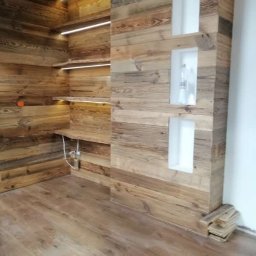 Stolkra - Drewniana zabudowa wnętrza z półkami podświetlonymi LED i wnękami w ścianie. Podłoga z paneli imitujących drewno. Wykończenie w rustykalnym stylu.